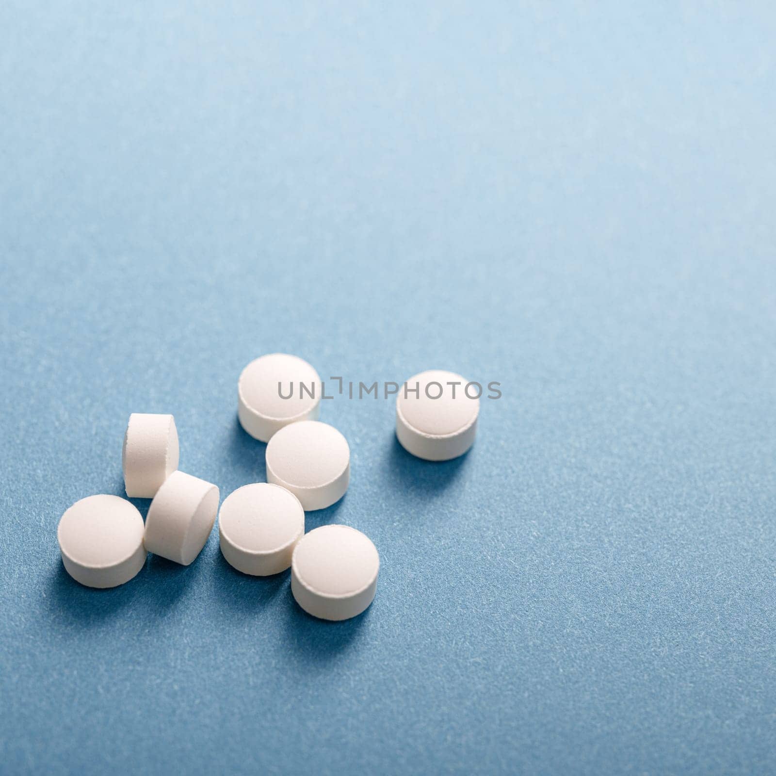 Handful of white medicinal tablets on blue background.