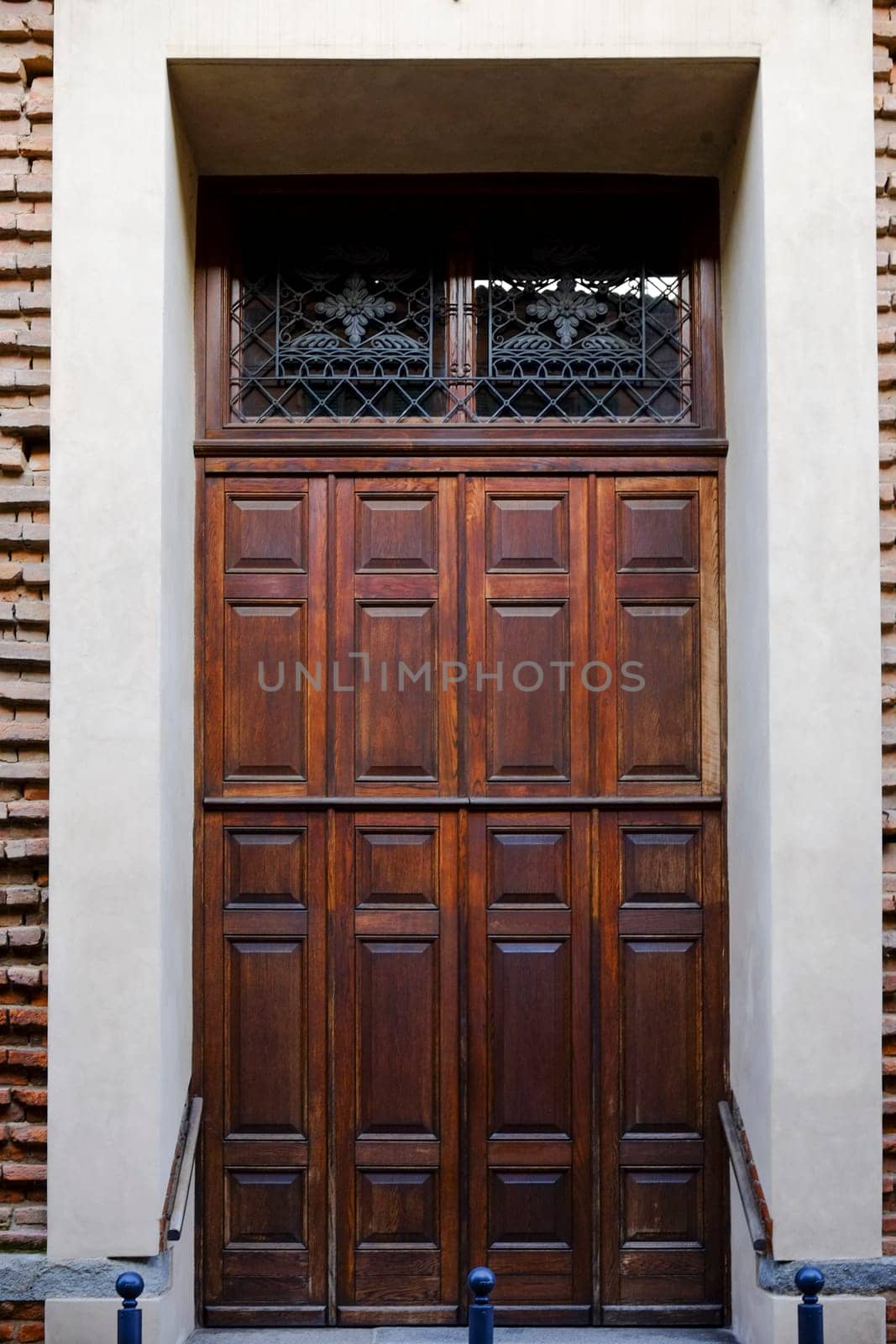 Cremona, Lombardy, Italy - November 7th 2024 Classic wooden door with decorative iron grate, set against a brick wall, showcasing timeless architectural design