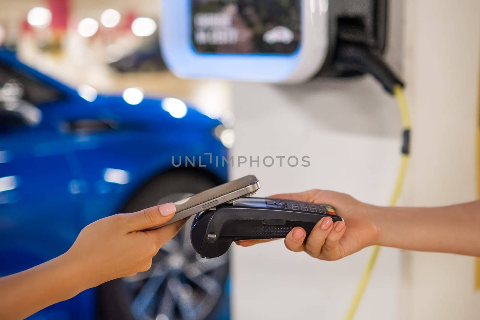Person makes a contactless payment at a terminal near a charging station with a mobile device.