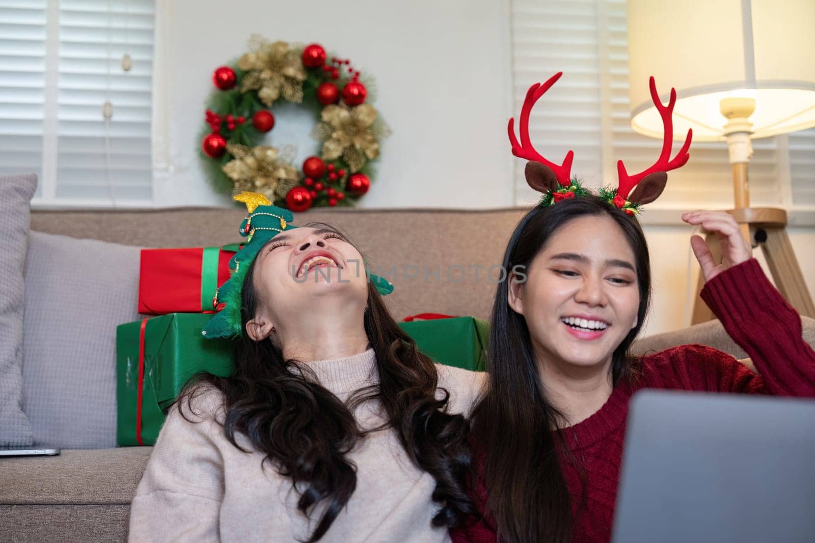 An interracial couple wearing festive antlers laughs joyfully while celebrating Christmas at home. Concept of togetherness, holiday spirit, and family fun.