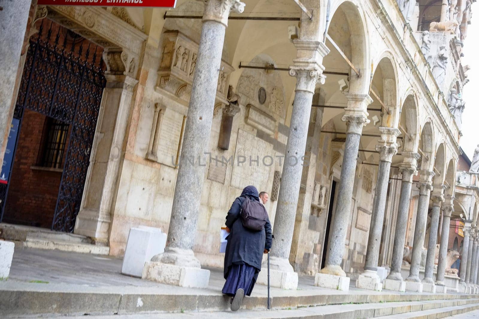 Cremona, Lombardy, Italy - November 7th 2024 Senior woman using a cane walking away under the arches of loggia di san giovanni in conca in milan, italy