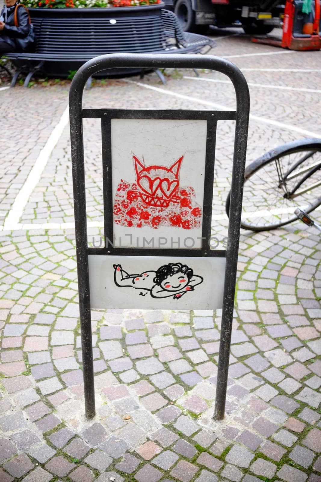 Cremona, Lombardy, Italy - November 7th 2024 Close-up of a metal sign featuring urban art depicting a cat and a lying baby, adding a touch of whimsy to a cobblestone street