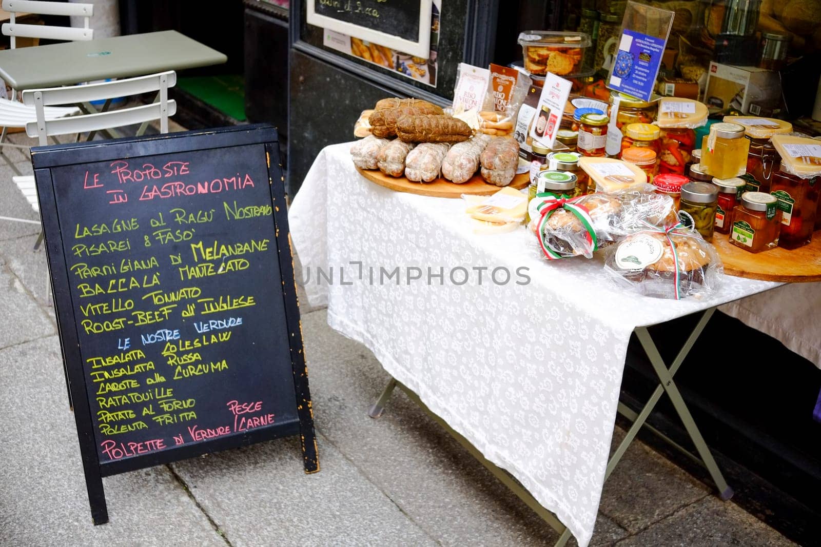 Cremona, Lombardy, Italy - November 7th 2024 Jars of preserves, sausages, and baked goods sit on a table covered with a white tablecloth next to a chalkboard menu written in italian