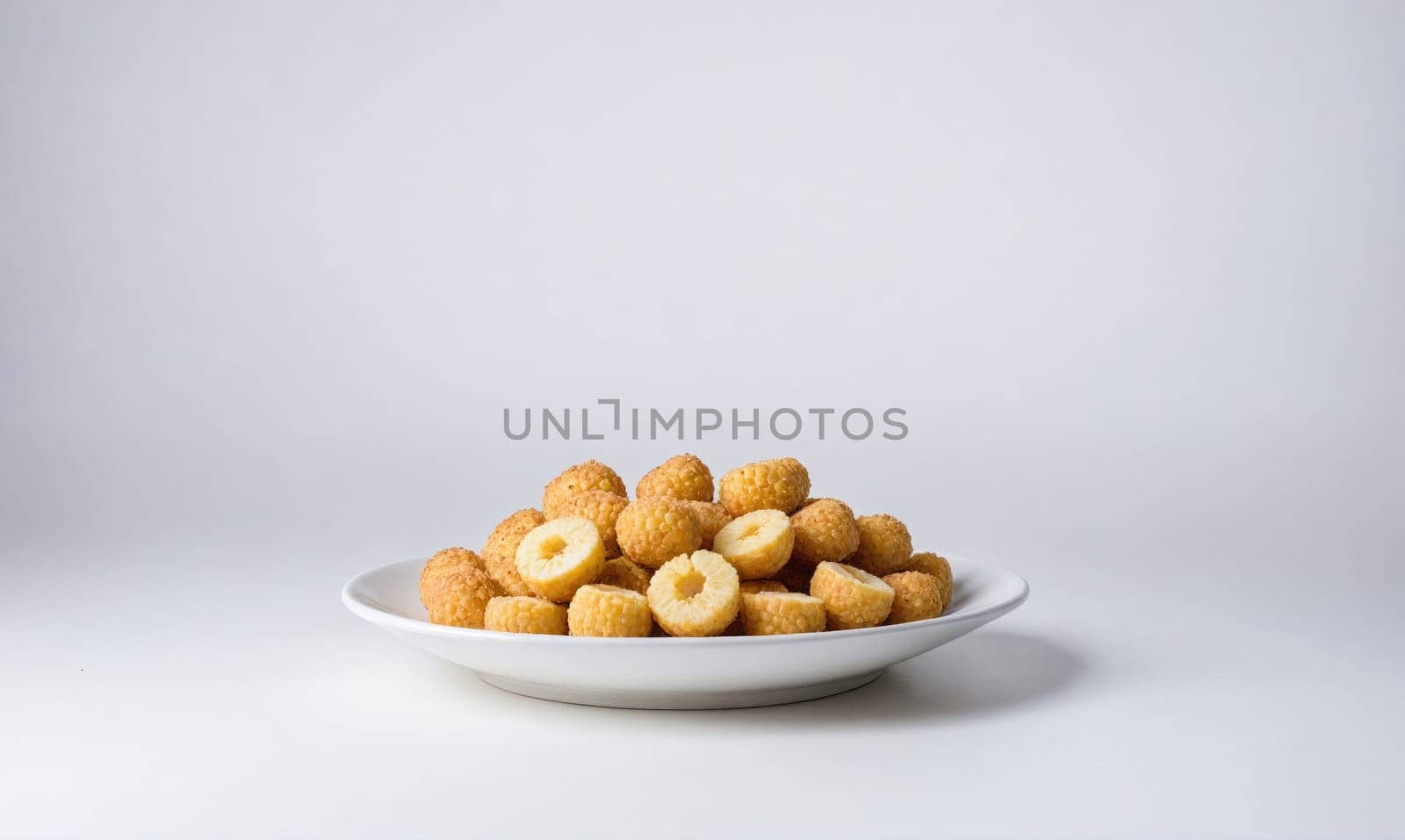 A pile of crispy, round snacks are arranged on a white plate and set against a white background. Some of the snacks are cut in half, revealing their yellow centers.