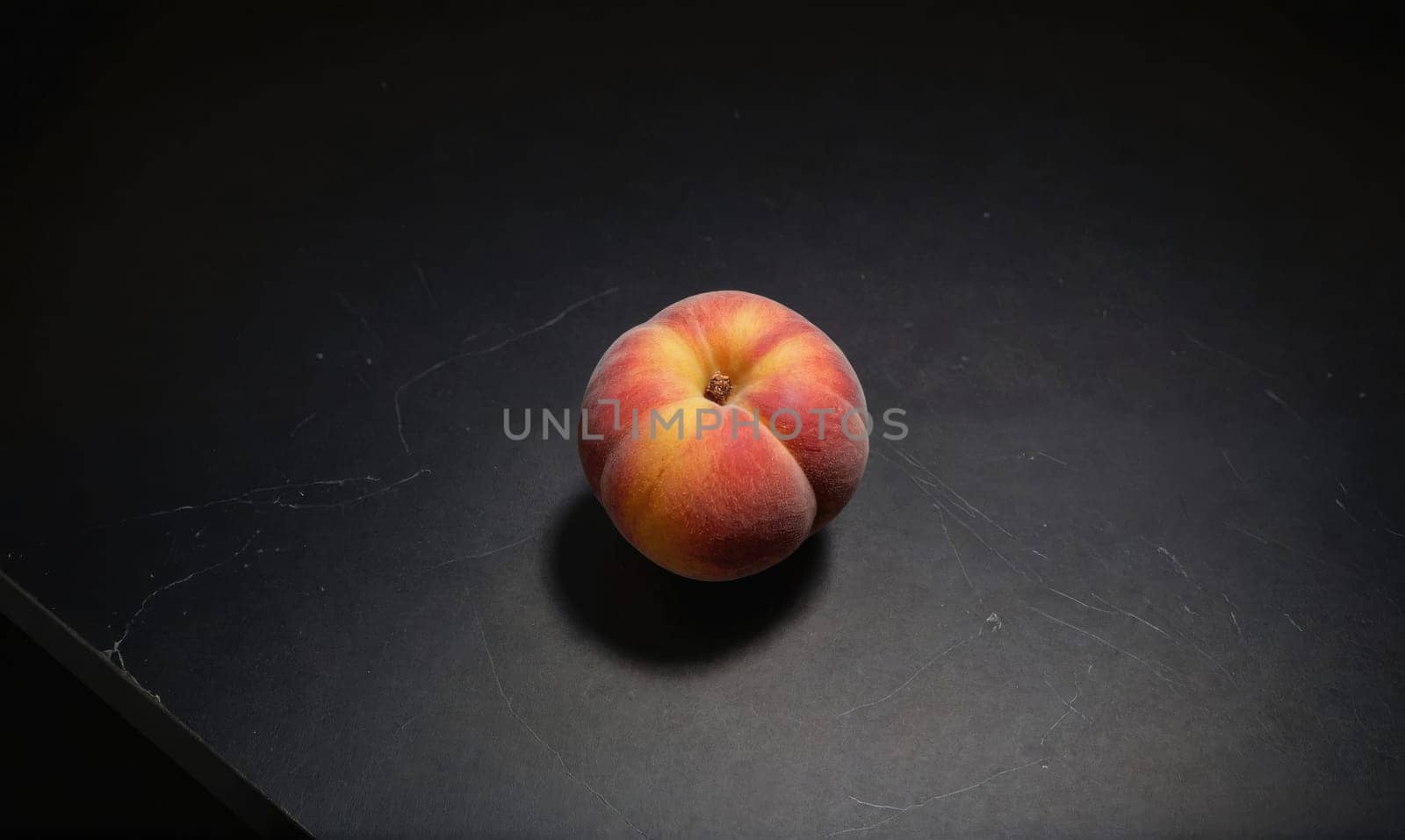 A peach sits on a black countertop. The peach has a dimpled surface and a slight blush of red on its skin.