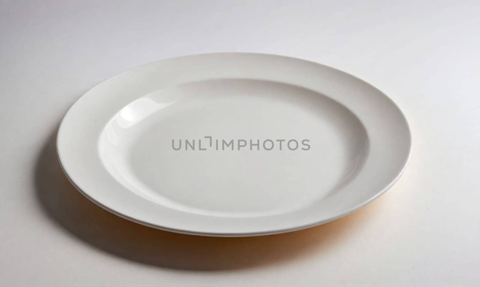 A clean, white dinner plate with a slight rim sits on a white surface. A shadow is visible beneath the plate.