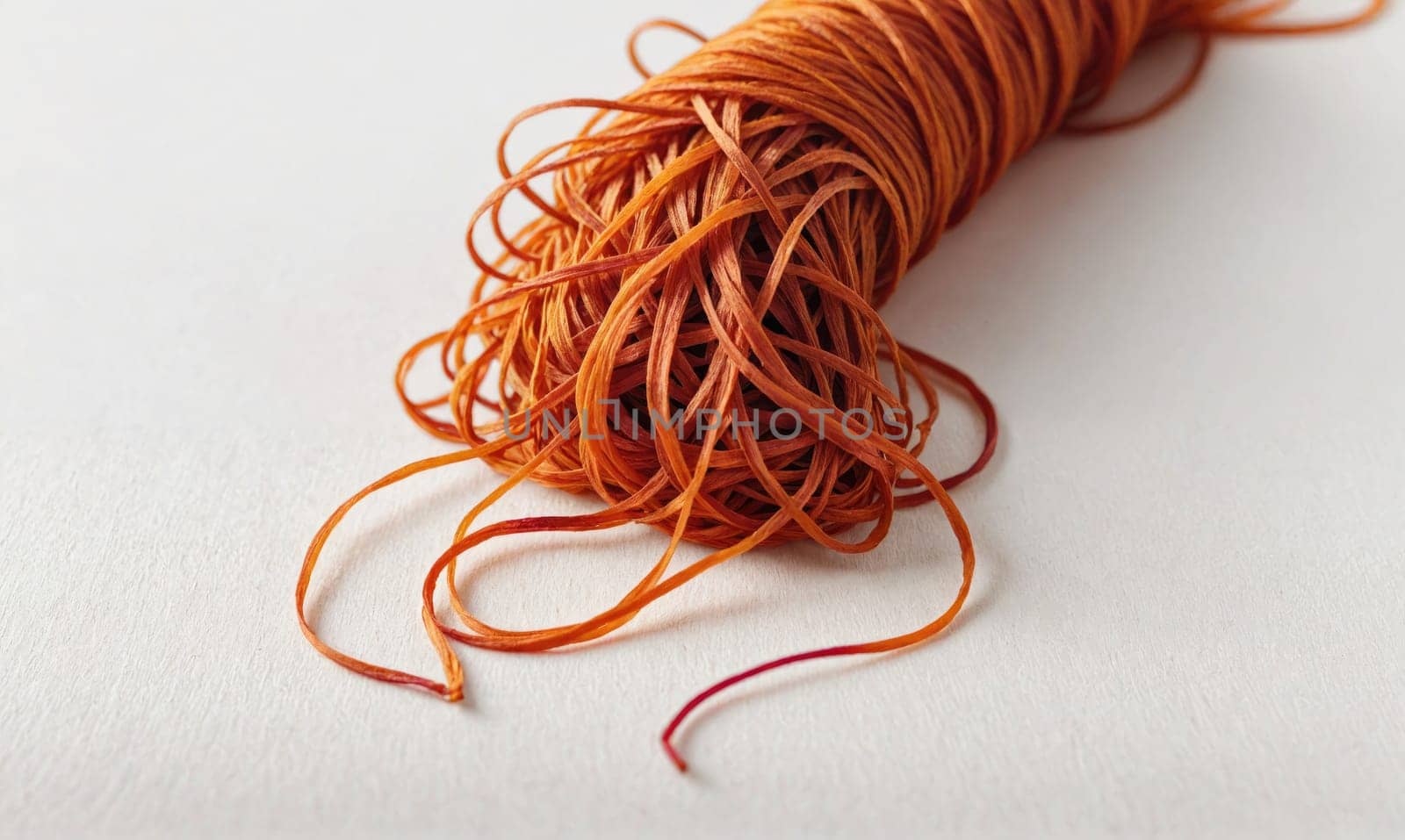 A tangle of orange twine sits on a white background. The twine is tightly wound and has a rough texture. The twine is unraveled in the bottom right corner of the image.