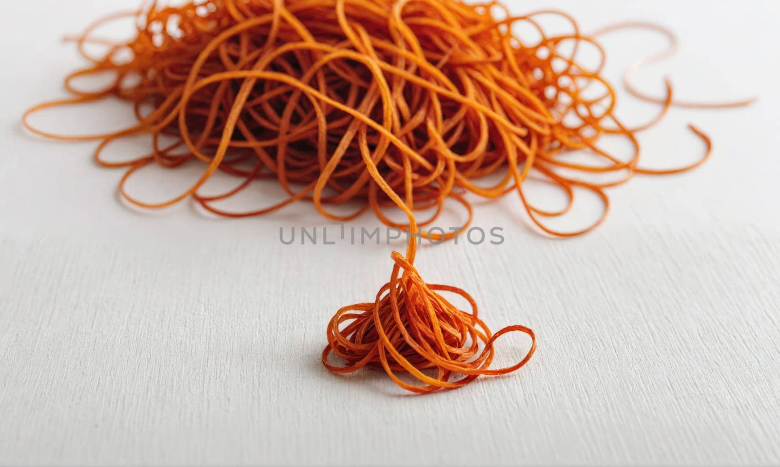A pile of orange rubber bands is scattered on a white surface. A small pile of rubber bands sits apart from the larger pile.