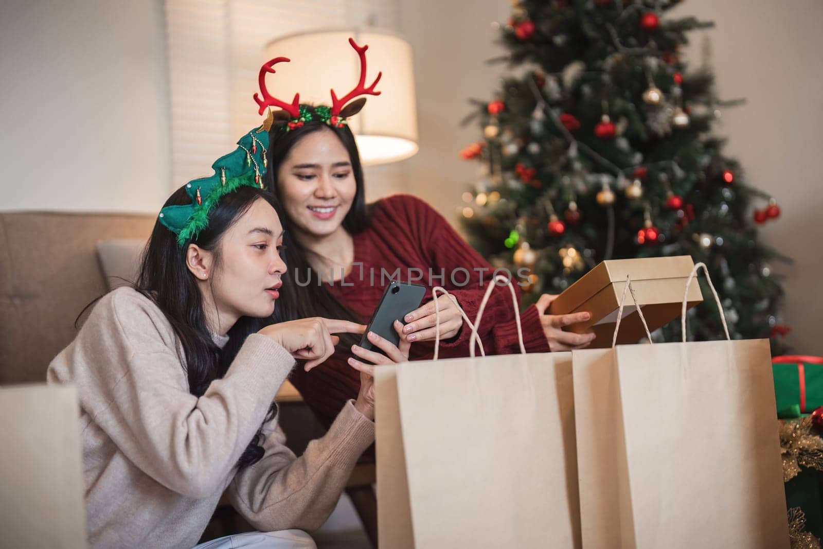 Lesbian friends share tech insights and exchange gifts in a decorated room, enjoying the seasonal spirit and company of each other.