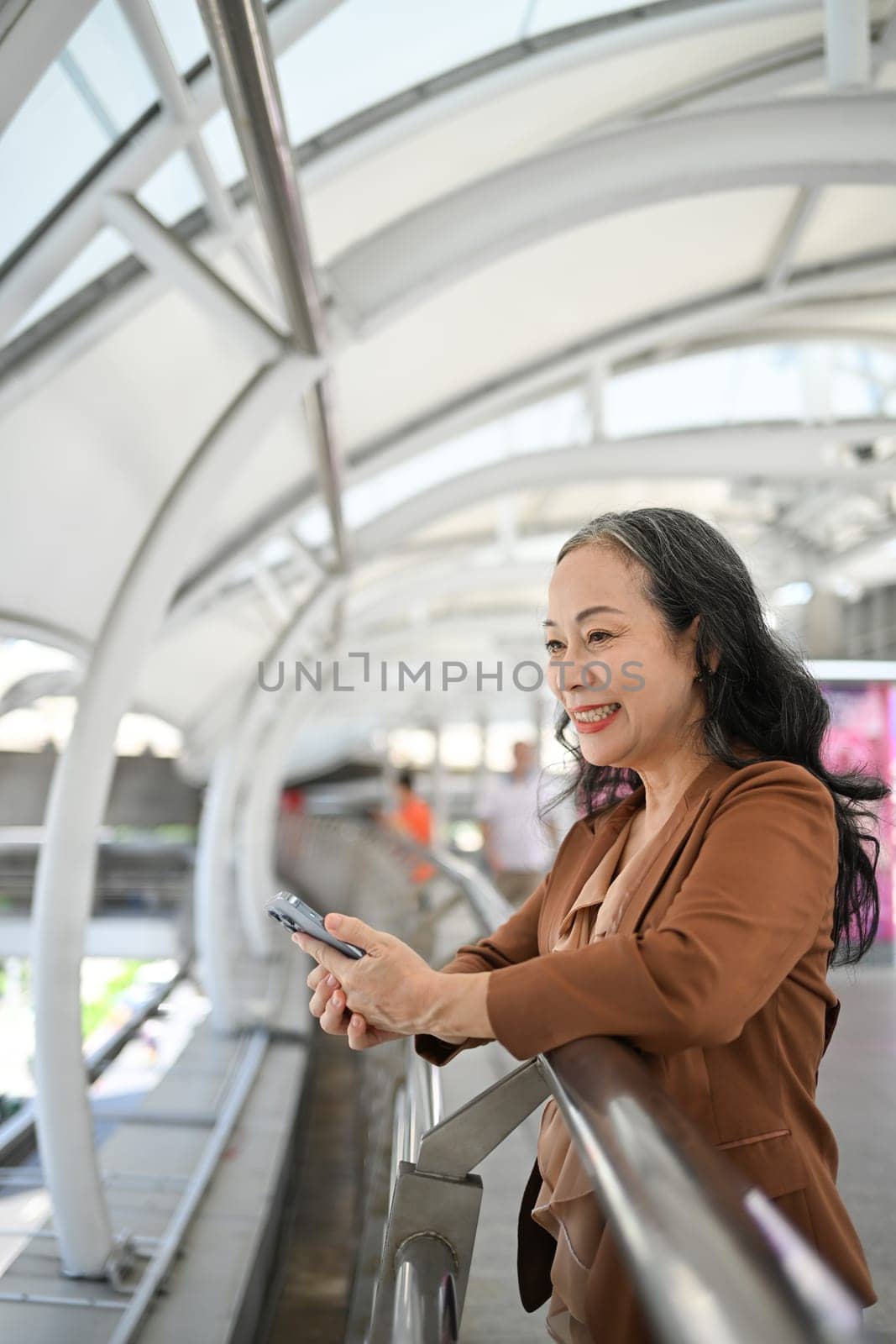 Smiling mature woman using smartphone in a busy urban space.