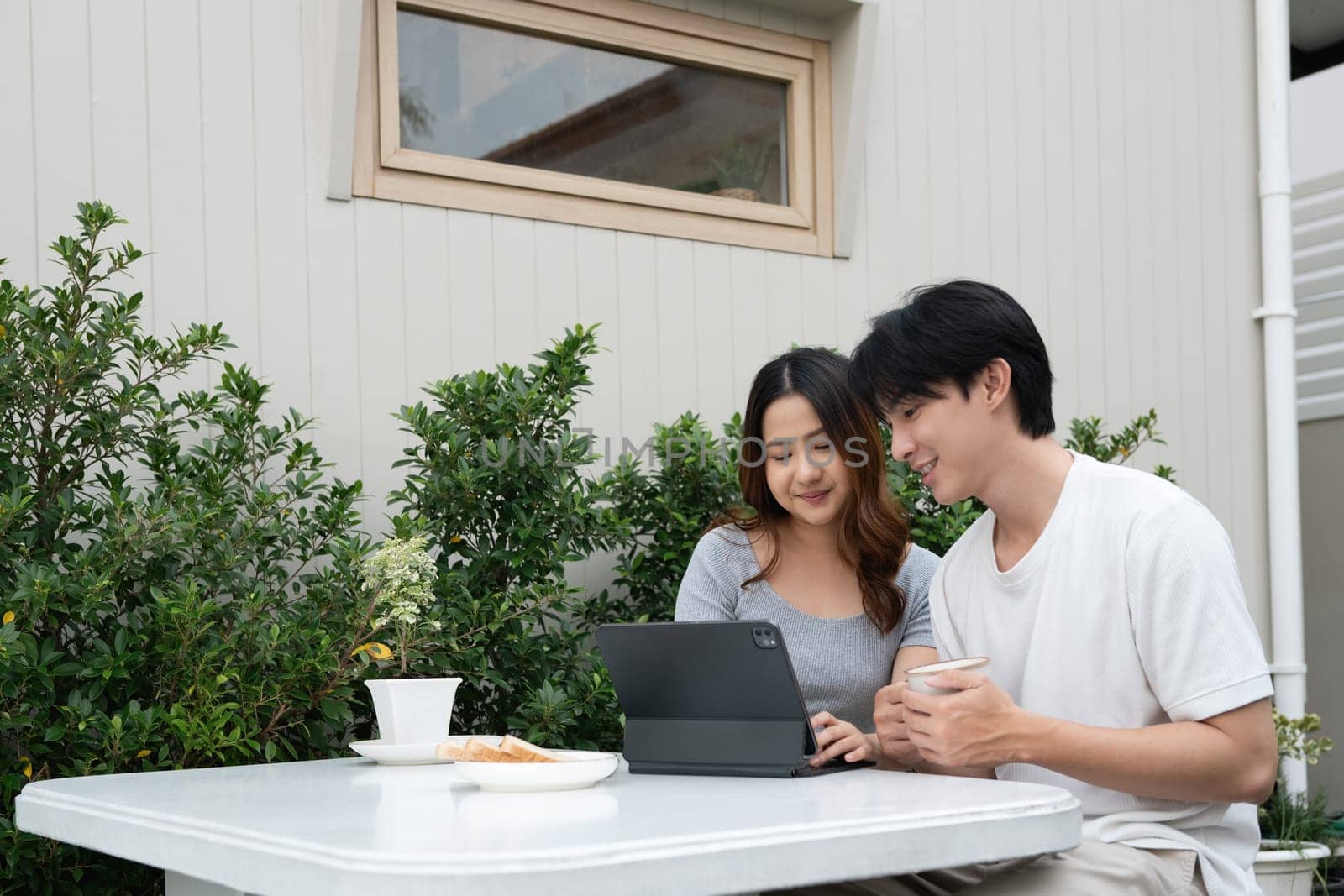 Happy asian couple sharing moments and using digital tablet in garden.