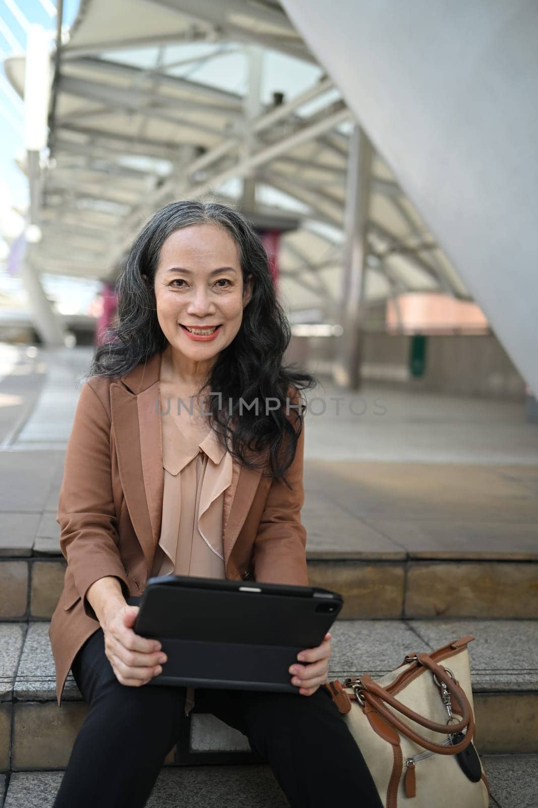 Smiling mature businesswoman working on digital tablet in urban area.