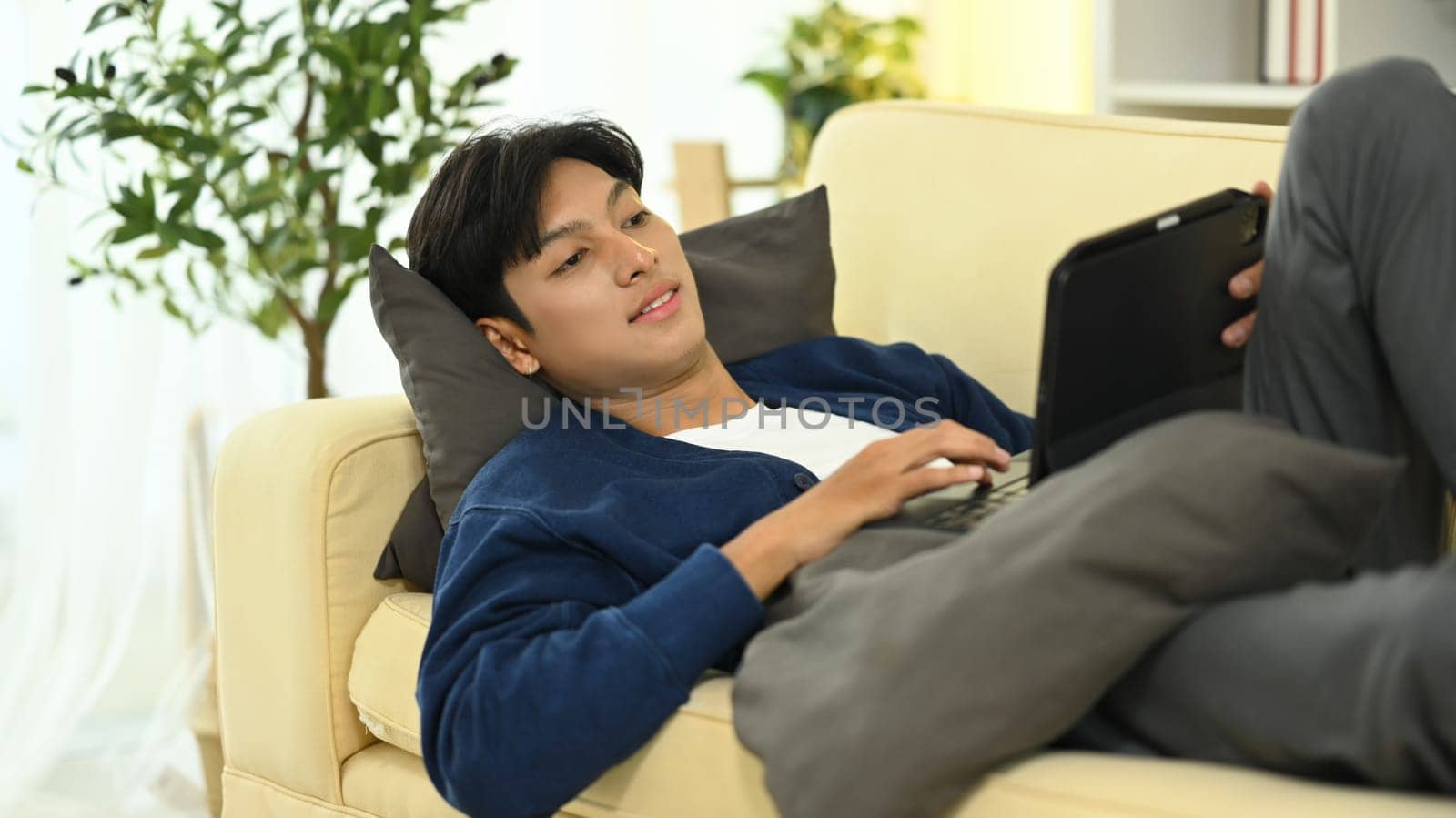 Handsome young asian man laying on sofa with digital tablet.