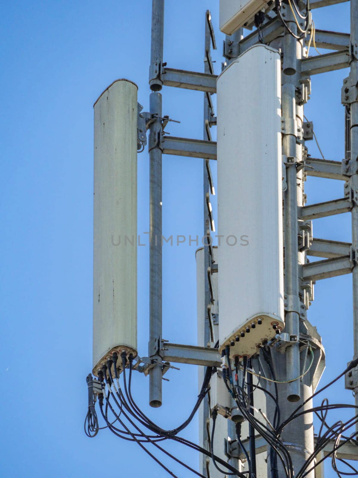 Sector antennas and microwave radio relay link equipment are installed on a telecommunication tower, providing wireless communication services against a clear blue sky