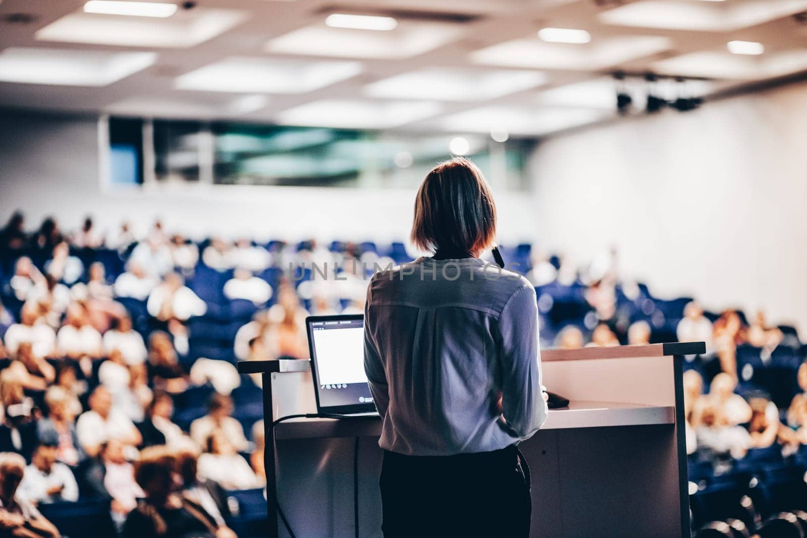 Female speaker giving a talk on corporate business conference. Unrecognizable people in audience at conference hall. Business and Entrepreneurship event