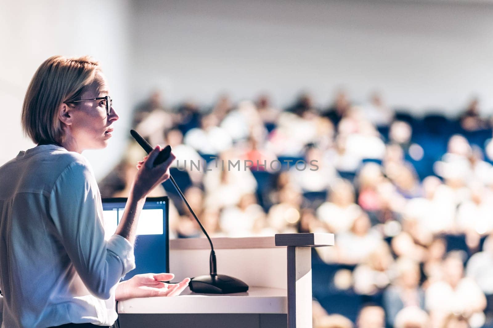 Female speaker giving a talk on corporate business conference. Unrecognizable people in audience at conference hall. Business and Entrepreneurship event