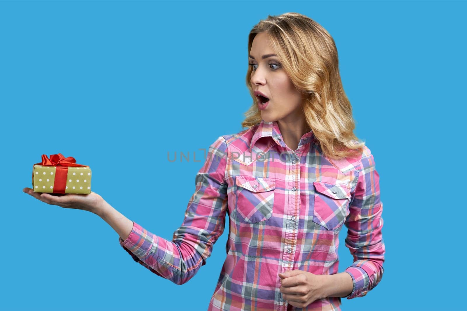 Excited young caucasian woman is holding gift box. Isolated on vivid blue background.