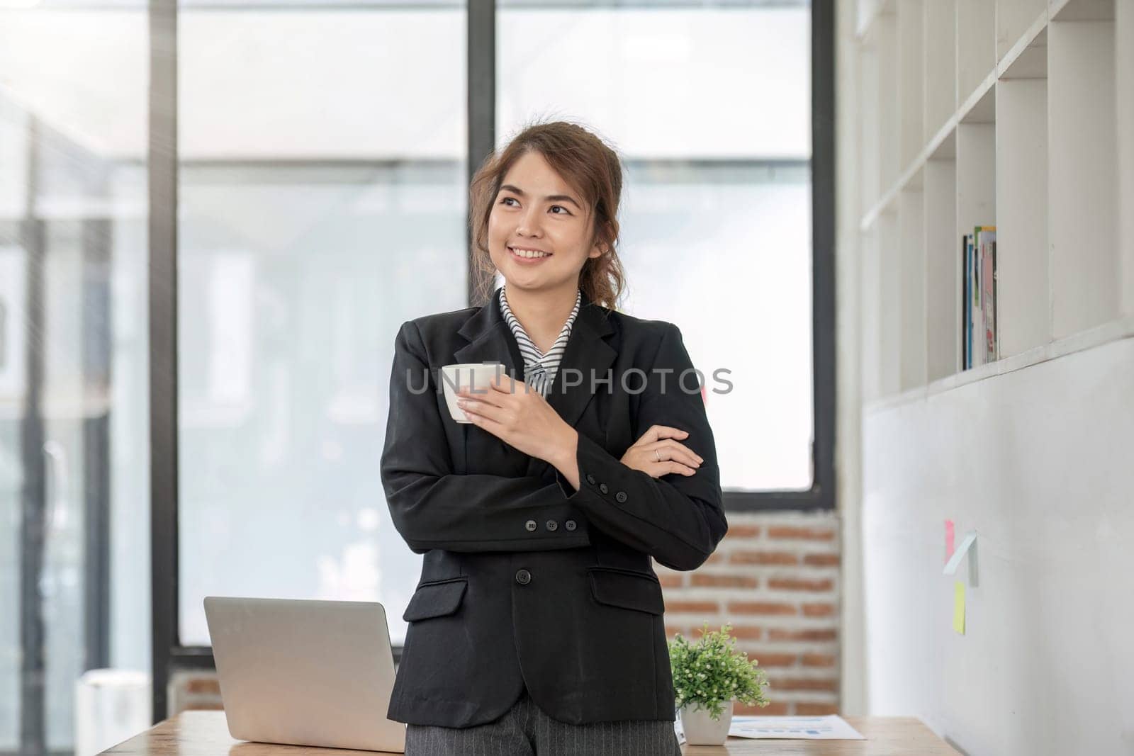 Portrait, Confident smiling asian businesswoman in suit standing in office with arms folded and holding coffee cup..