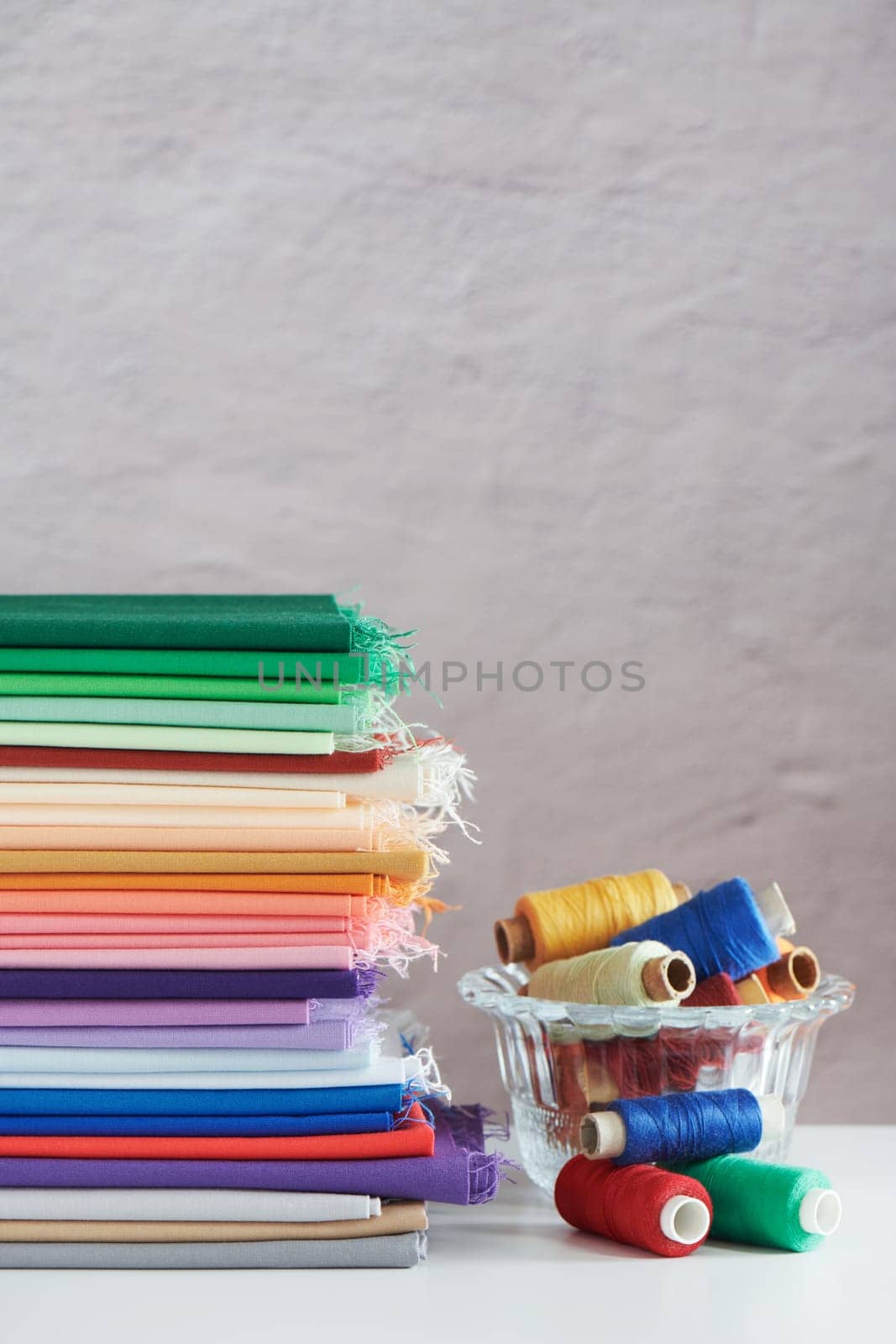 Stack of colorful monochromatic fabrics and spools of thread on grey  background, space for text