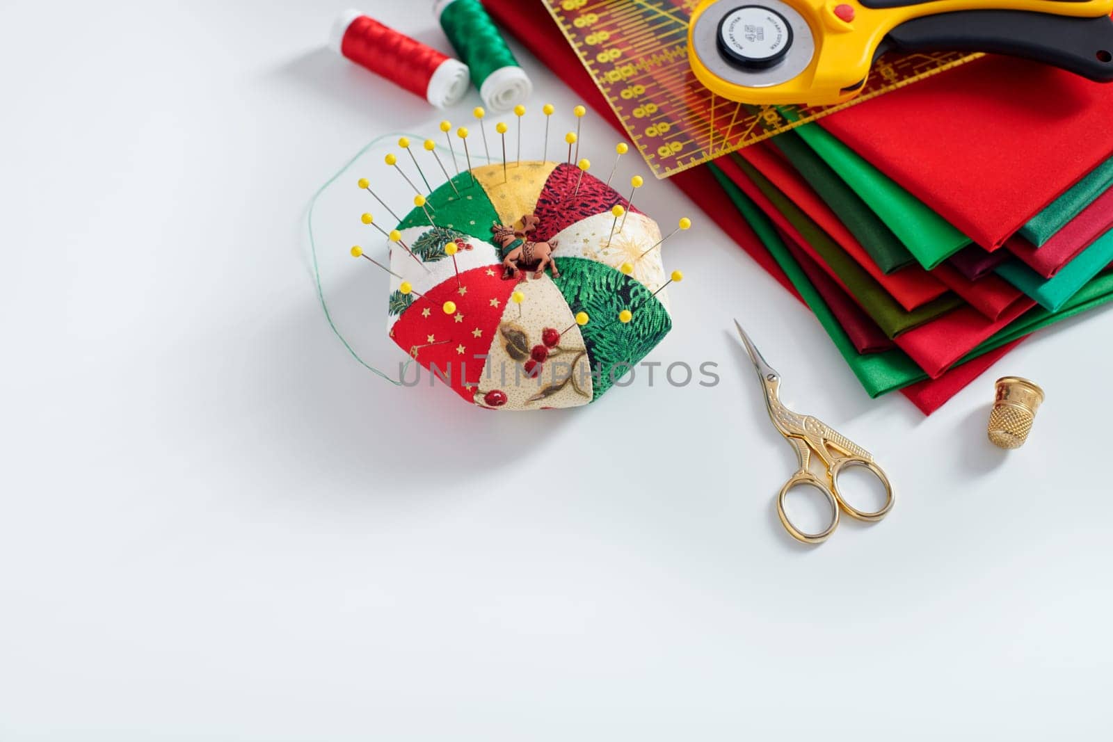 Pile of red and green fabrics, pincushion, sewing and quilting accessories on white background, space for text