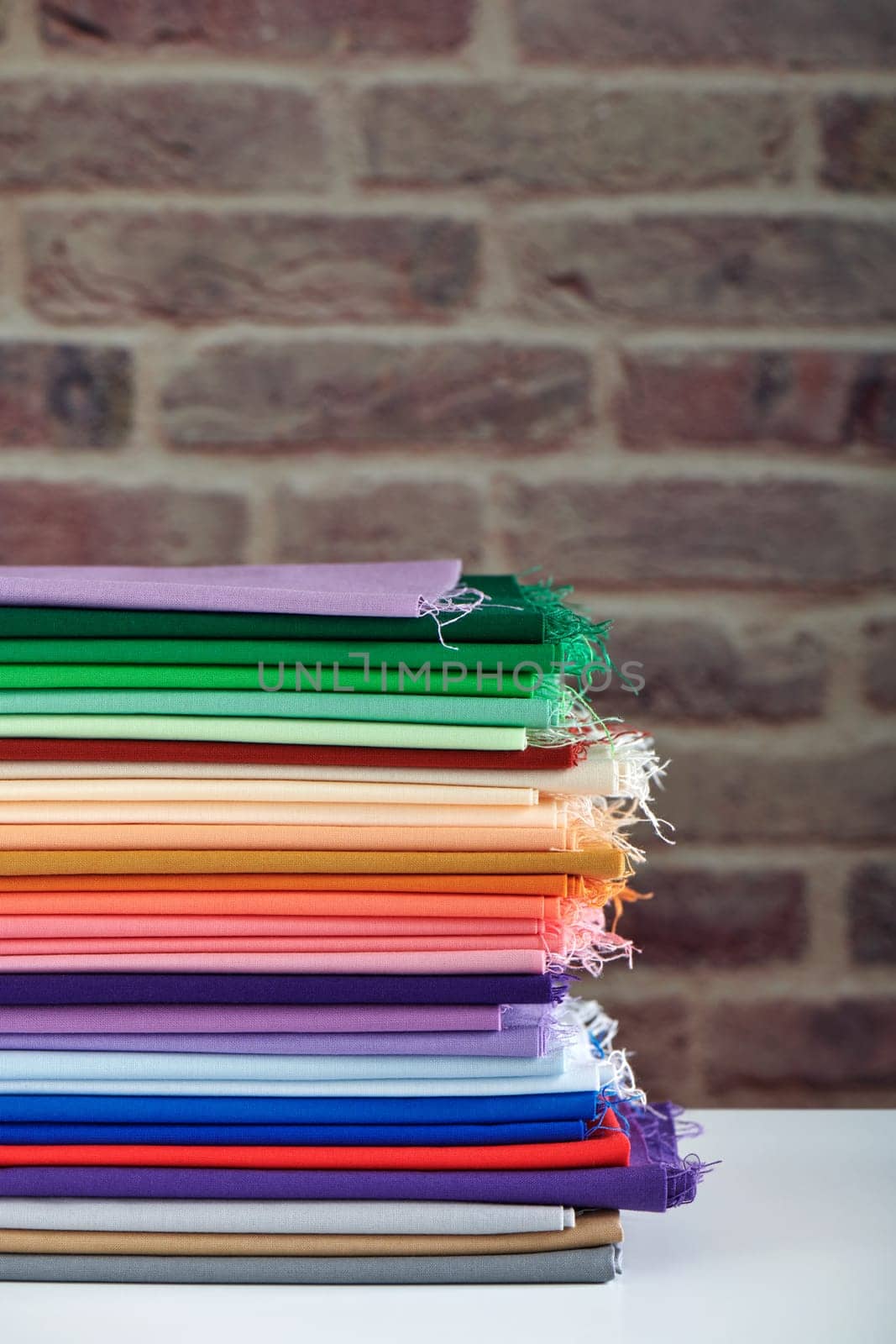Stack of colorful fabrics on brick wall background, space for text