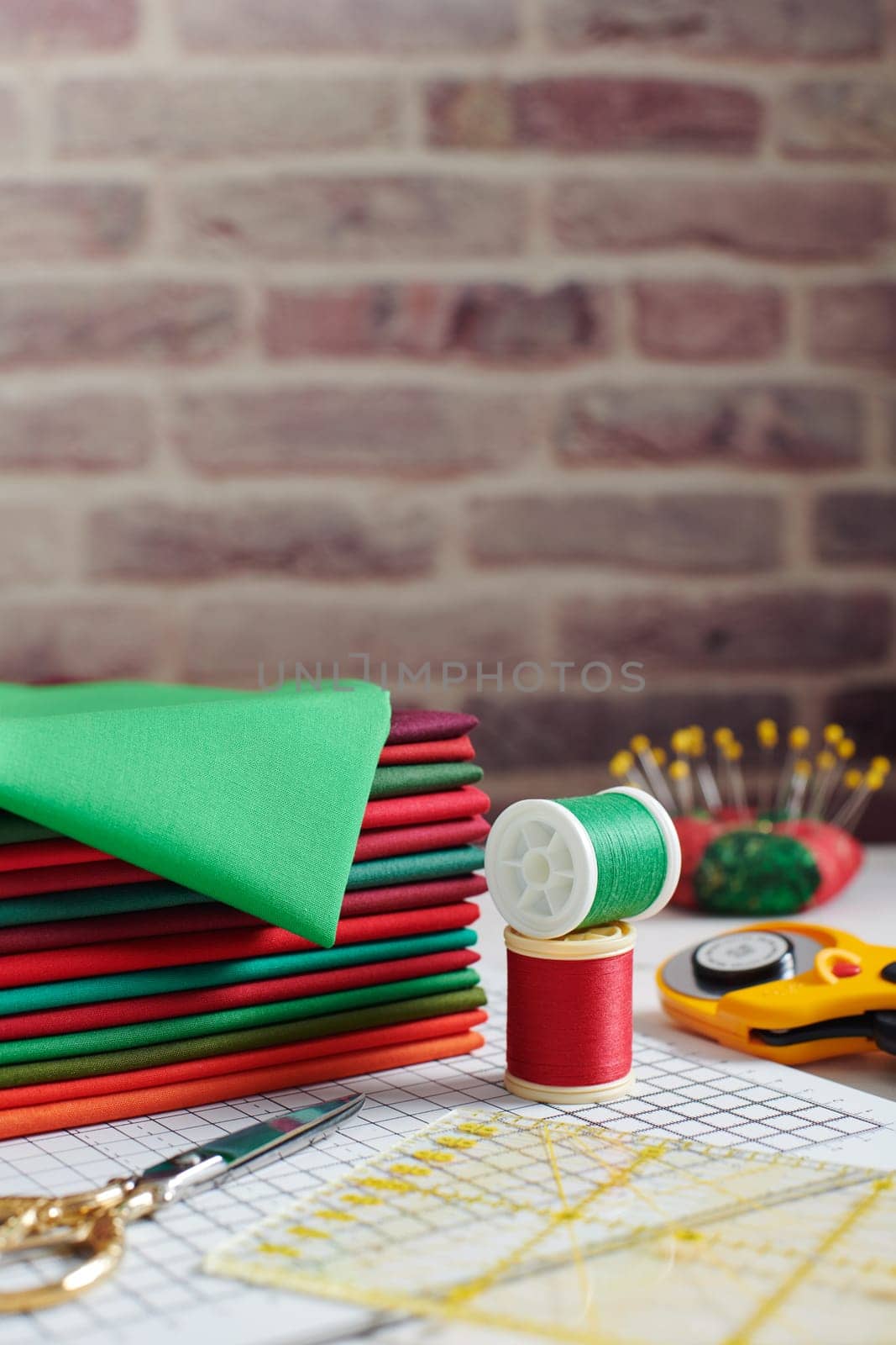 Stack of red and green fabrics surrounded by sewing and quilting accessories on brick wall background
