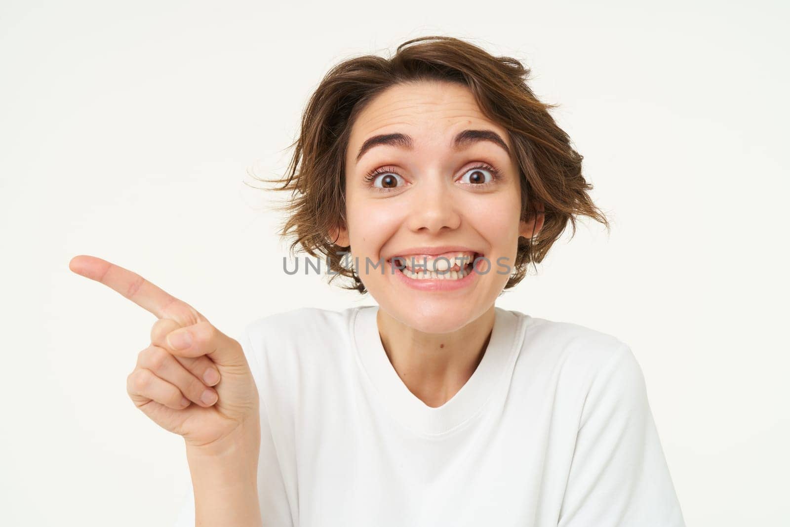 Image of candid brunette girl, pointing left, showing advertisement, recommending store, standing over white background. copy space