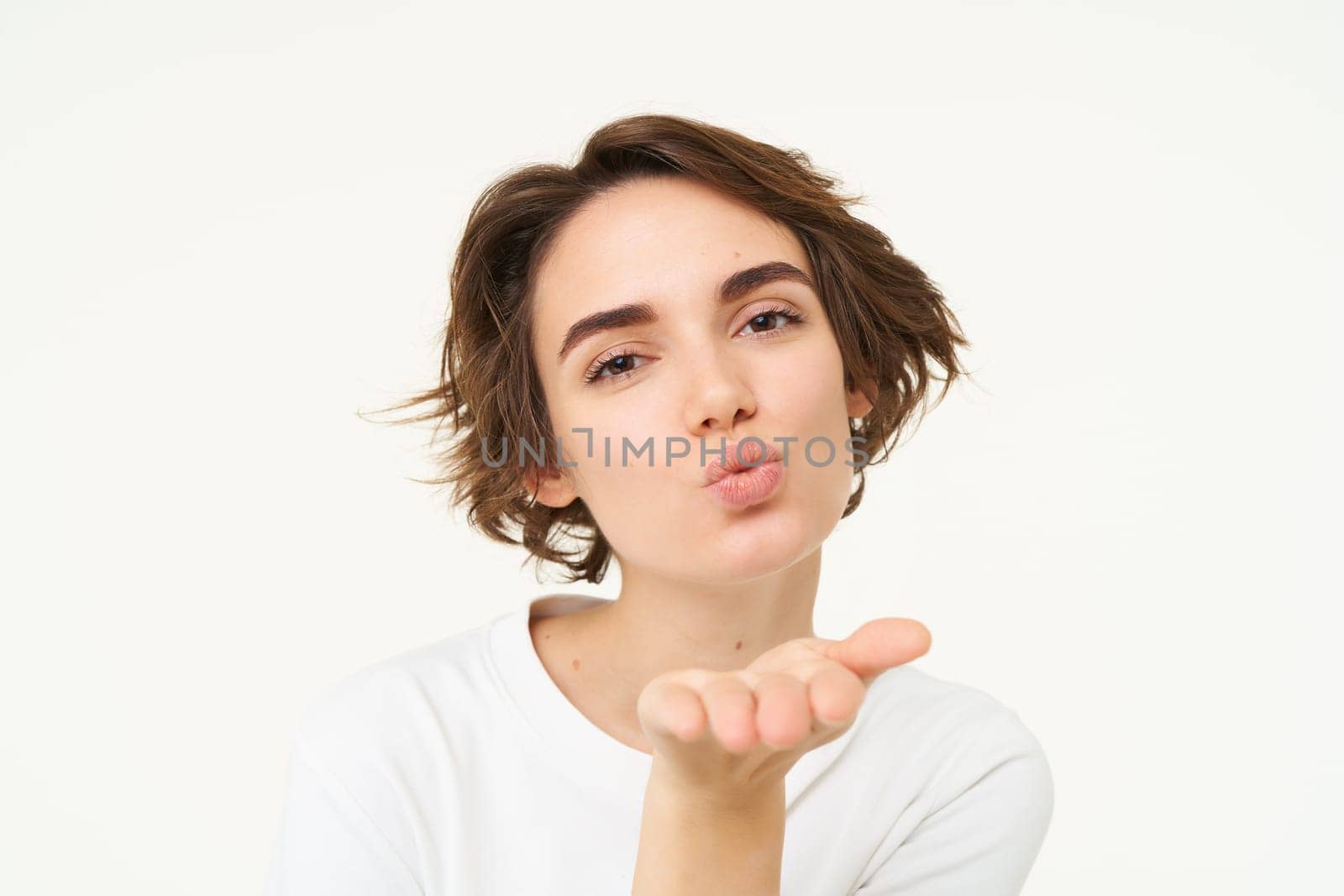 Close up of brunette woman, sending air kiss at camera, posing over white background by Benzoix