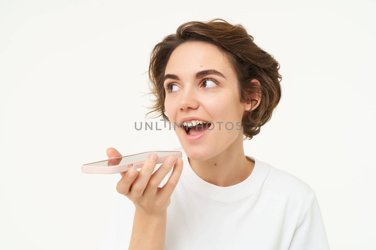 Portrait of woman talking into mobile phone speakerphone, records voice message, translates words, stands over white background by Benzoix