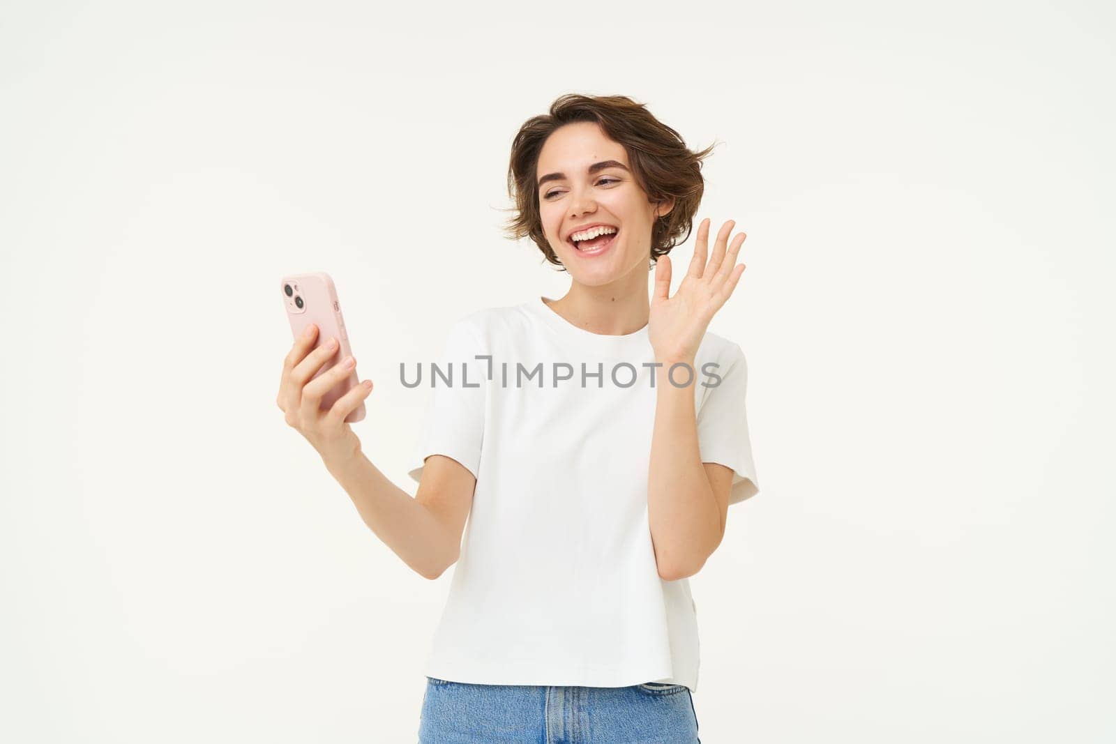 Portrait of girl talking on mobile phone, video chats with friends on smartphone, standing over white studio background.