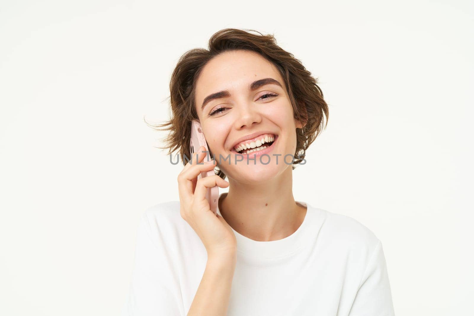 Portrait of happy, chatty young woman talking on mobile phone, using smartphone, calling someone, standing over white studio background by Benzoix