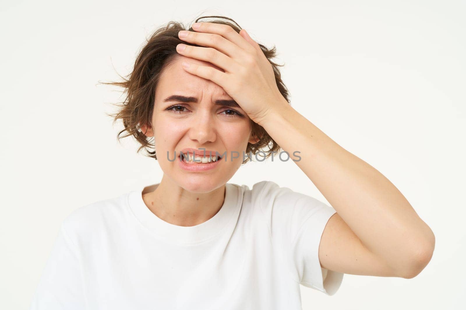 Portrait of woman touches her head, looks upset or disappointed, forgot something, has headache, migraine, standing over white background.