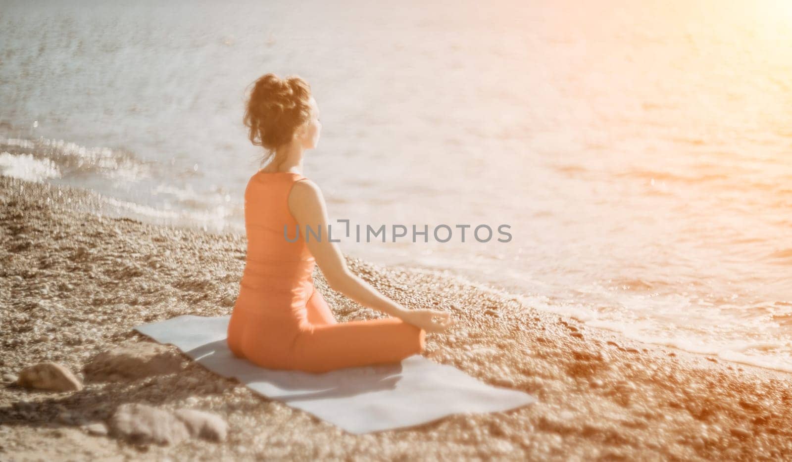 Woman sea yoga. Selective focus. Young beautiful caucasian woman in a red suit practicing yoga on the beach at sunrise near the sea. Yoga. Healthy lifestyle. Meditation concept. by panophotograph