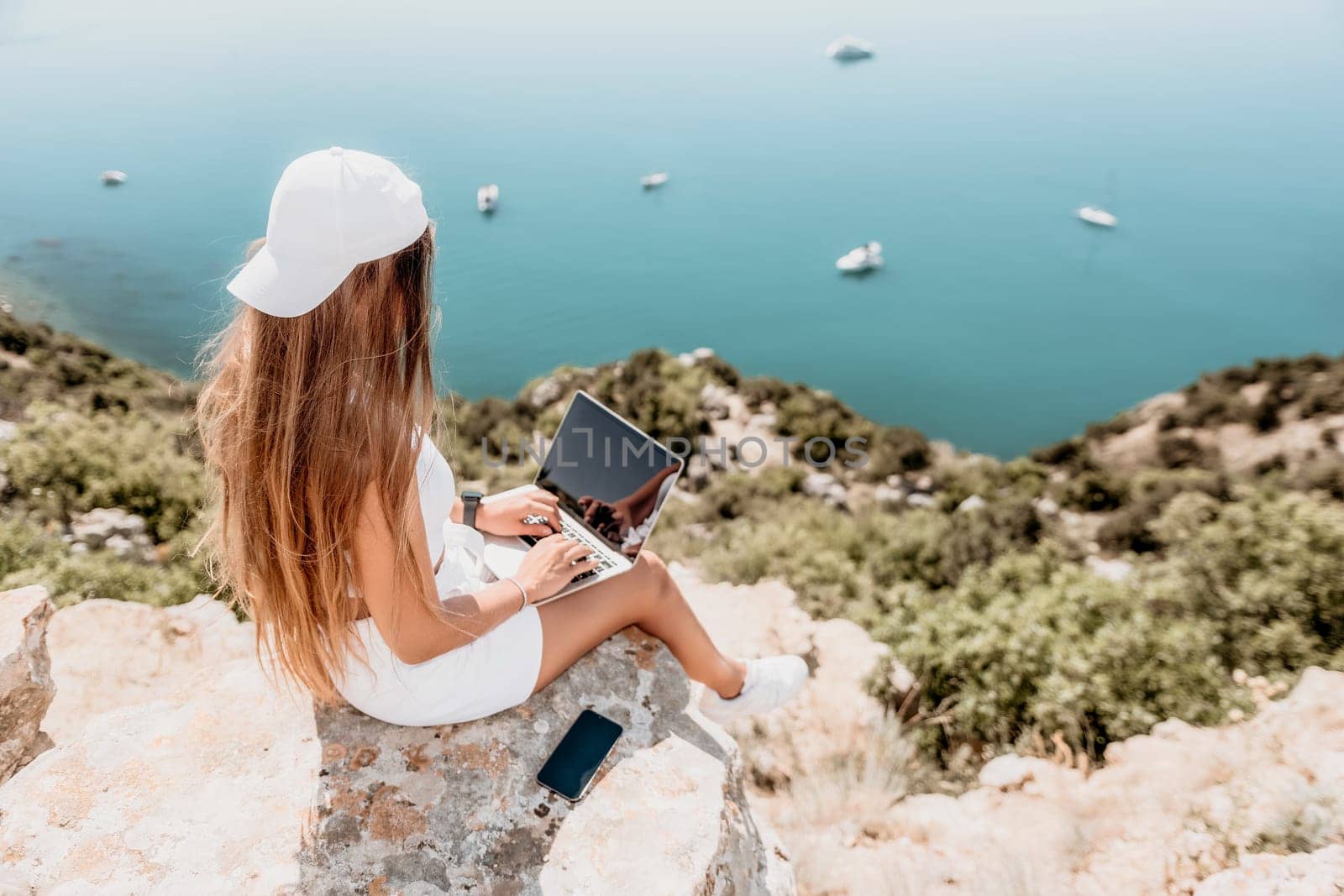 Digital nomad, Business woman working on laptop by the sea. Pretty lady typing on computer by the sea at sunset, makes a business transaction online from a distance. Freelance remote work on vacation