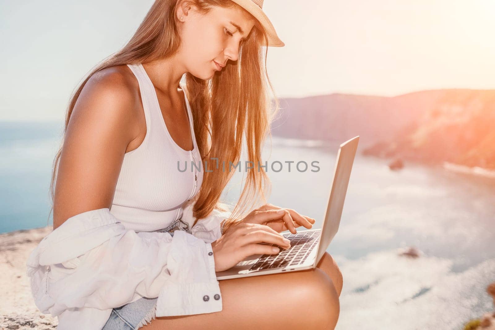 Woman sea laptop. Business woman in yellow hat freelancer with laptop working over blue sea beach. Girl relieves stress from work. Freelance, digital nomad, travel and holidays concept by panophotograph