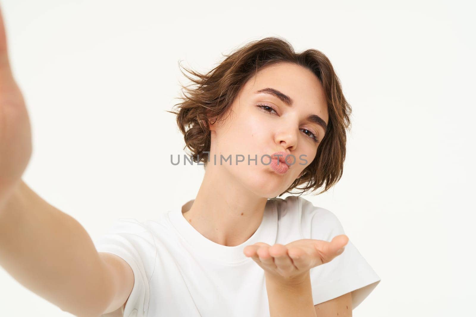 Close up of smiling brunette woman makes selfie, taking photo for her social media, holds mobile phone with extended hand, standing over white background by Benzoix