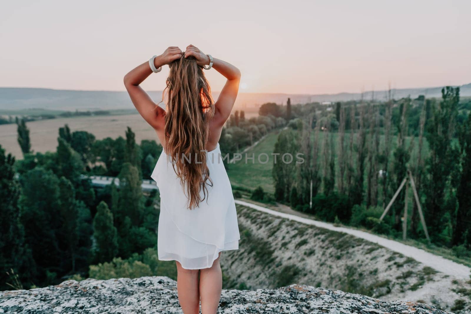 Romantic beautiful bride in white dress posing with sea and mountains in background. Stylish bride standing back on beautiful landscape of sea and mountains on sunset