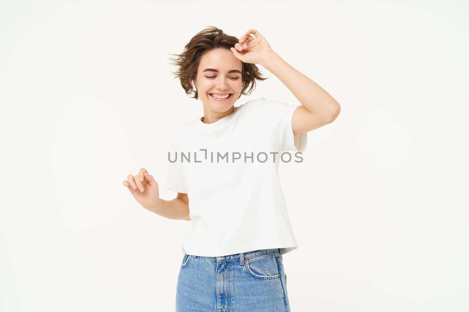 Carefree dancing girl having fun, listening music in wireless headphones, enjoying to move to the rhythm of favourite song, white background.