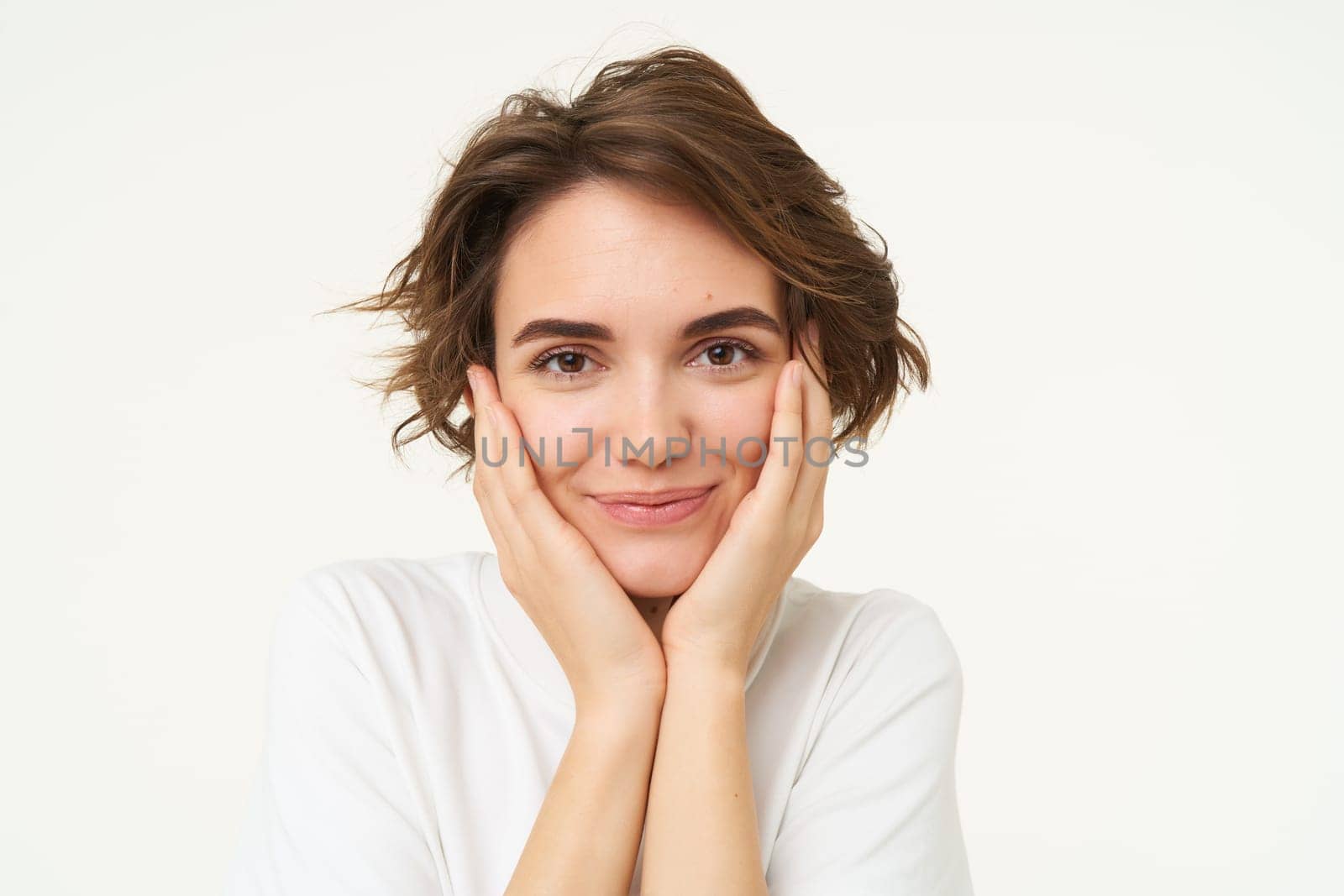 People and emotions concept. Young woman touches her face, smiling, pleased with her face condition after skincare treatment, stands over white background.