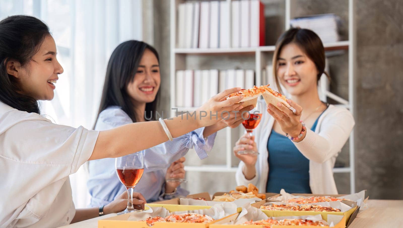 Group of Asian friends together to celebrate Christmas with champagne and eating pizza at home. Joy of holiday party with friends or colleague concept by wichayada