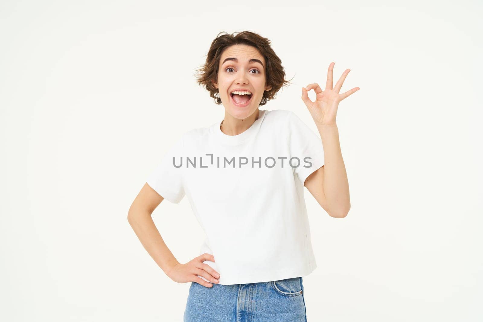 No problem. Portrait of young woman standing in confident pose, shows okay, ok, zero gesture, stands over white studio background.