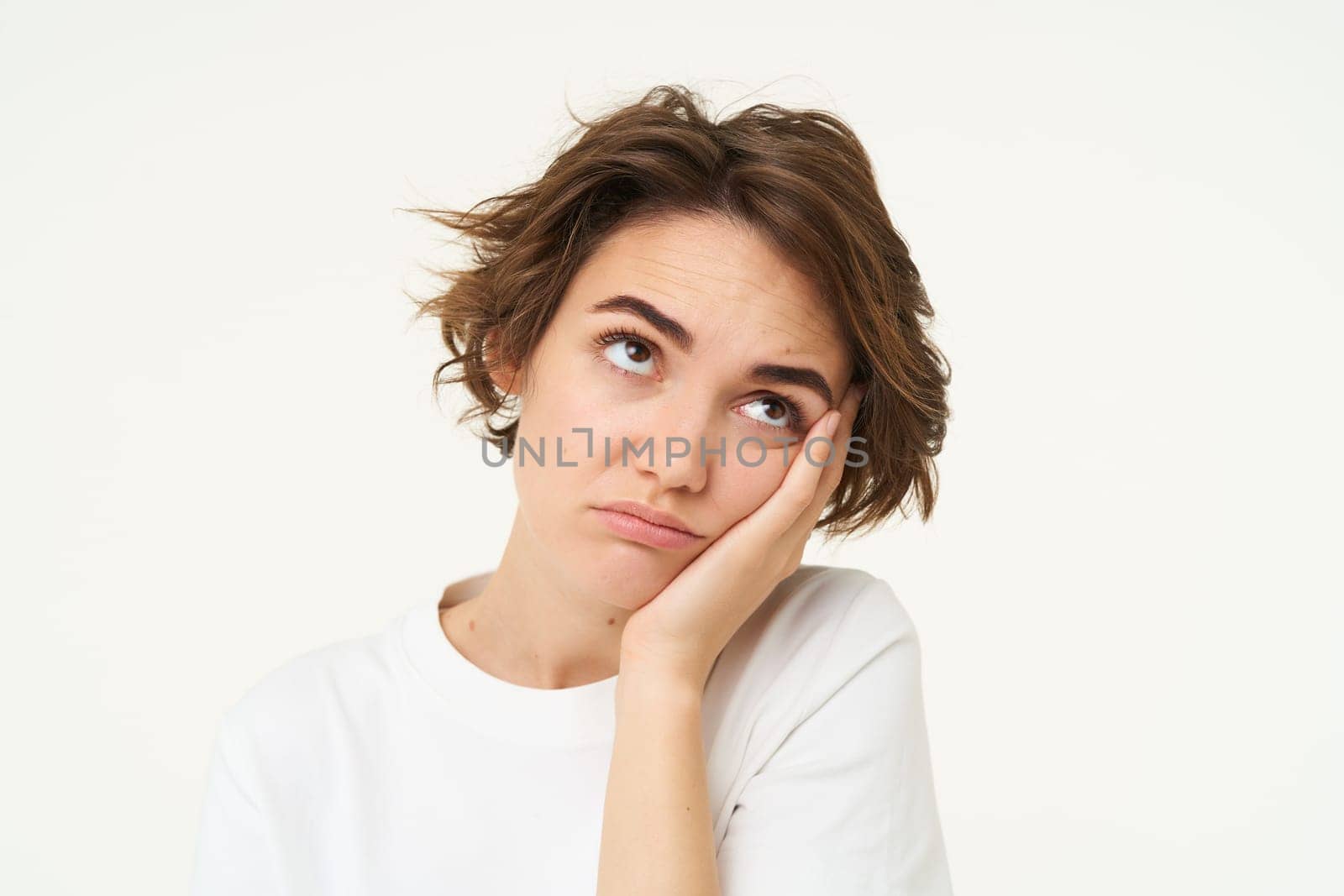 Close up of bored young woman, rolls her eyes, leans on hand and looks reluctant and upset, isolated over white background. Copy space