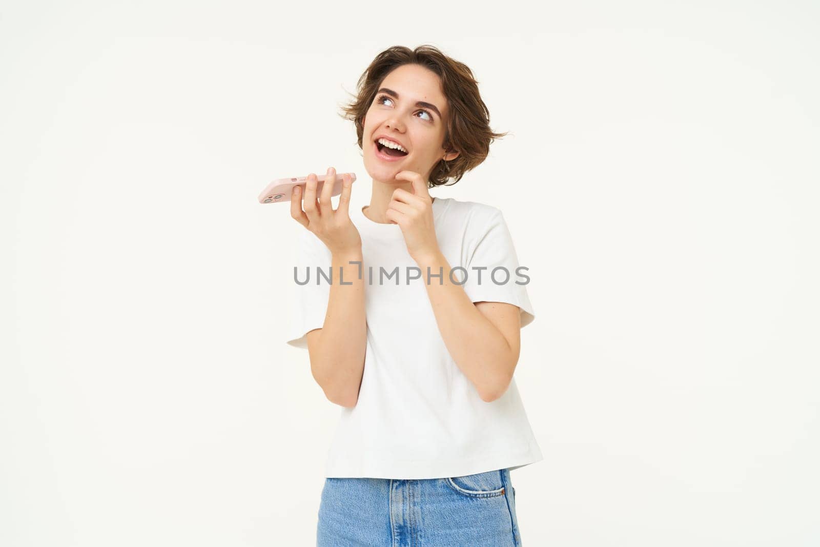 Portrait of brunette woman recording voice message, girl talking on mobile phone, using speakerphone, translating her words, standing over white background.