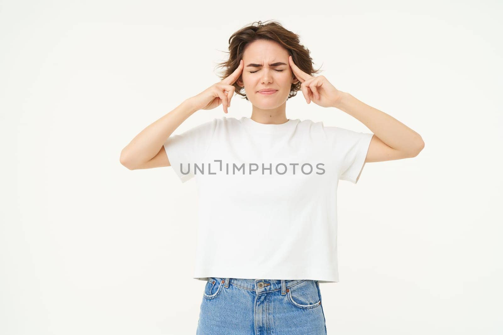 Image of brunette woman touches her head and frowns, looks anxious, thinking, trying to remember, looking worried and concerned, standing over white background.