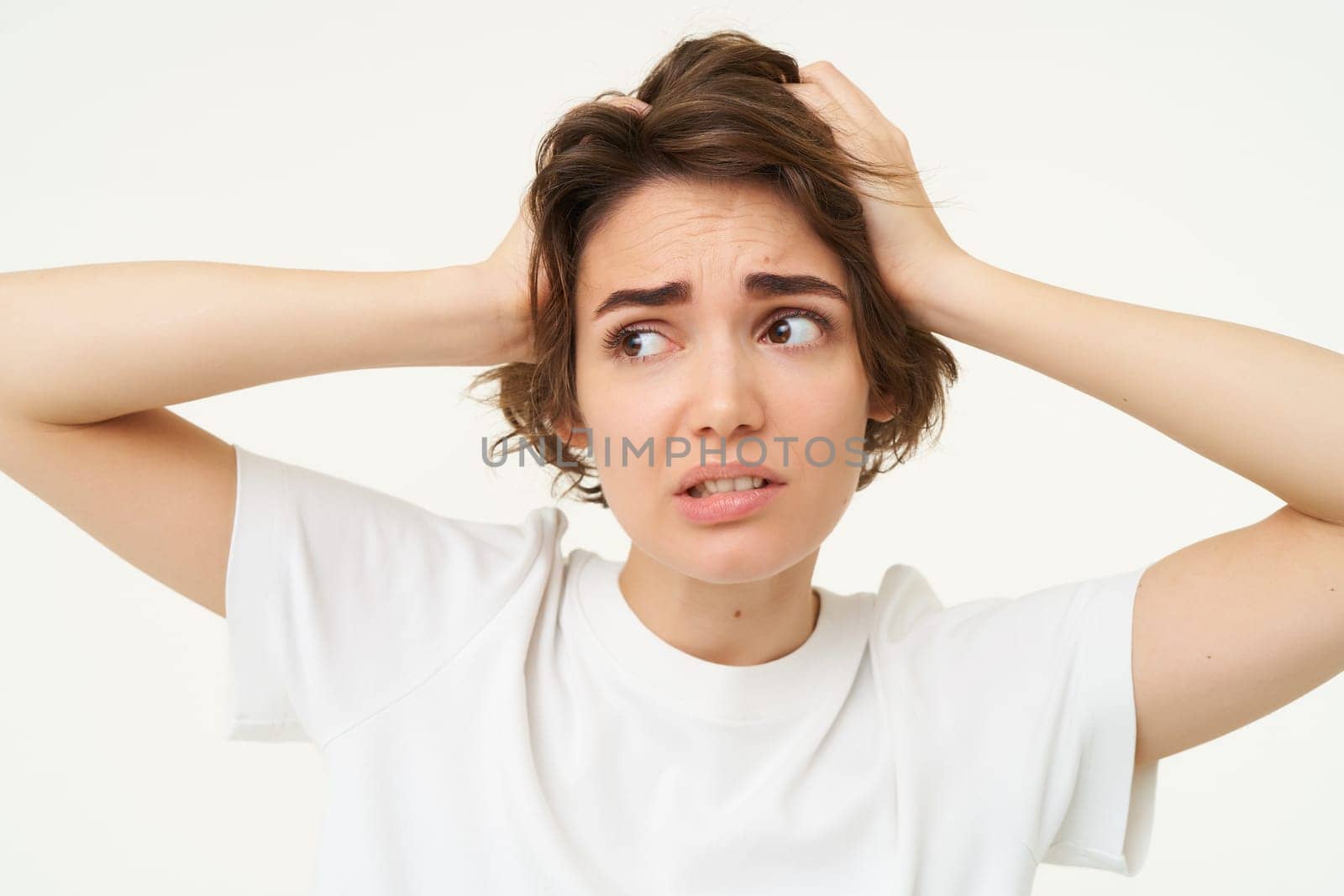 Close up of girl in panic, looking around, holding hands on head, facing trouble, complicated issue, standing over white background.