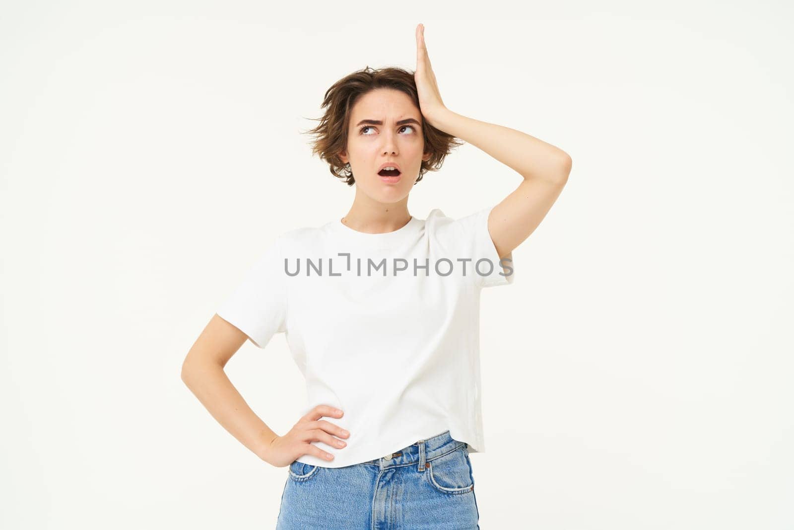 Portrait of forgetful woman, touches her head, remember something important, looks upset or shocked, stands over white background.