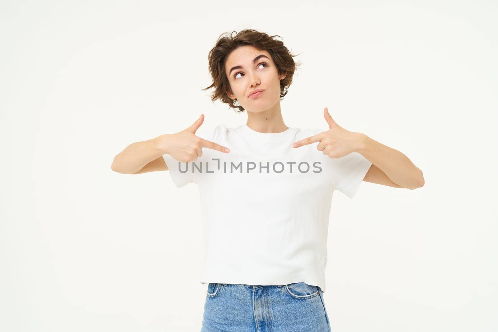 Portrait of thoughtful girl, pointing at herself and looking up, thinking, dreaming, posing over white studio background.