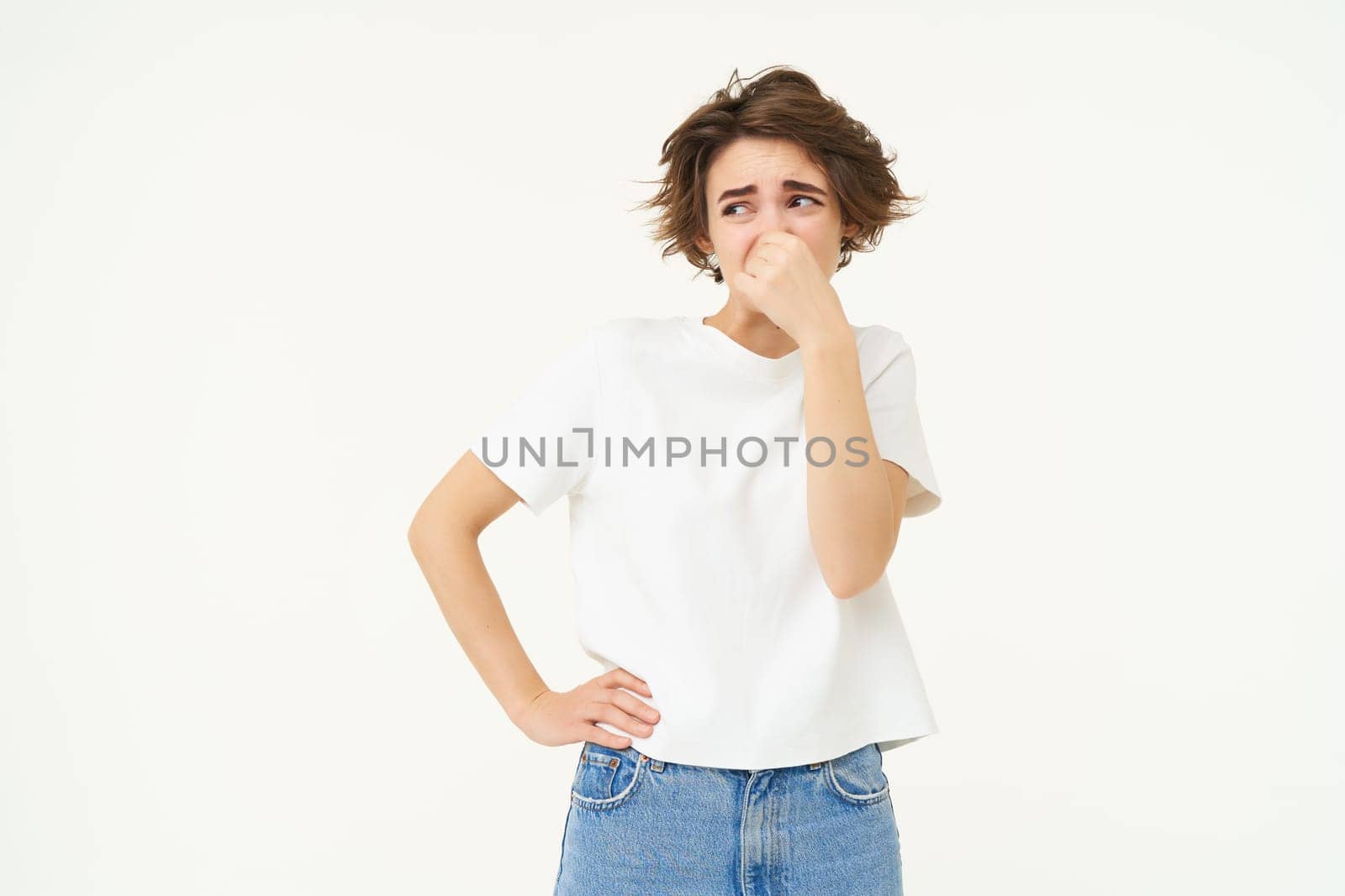 Portrait of woman disgusted by bad smell, shuts her nose, stands over white studio background by Benzoix