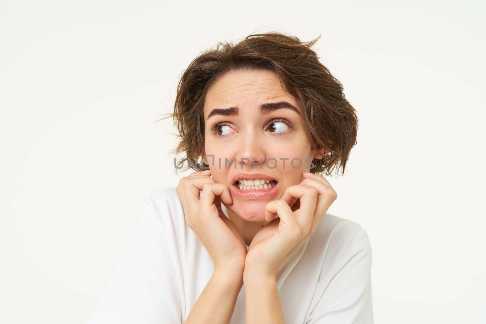 Close up of scared brunette woman, shaking from fear, looking concerned and frightened, standing over white studio background by Benzoix