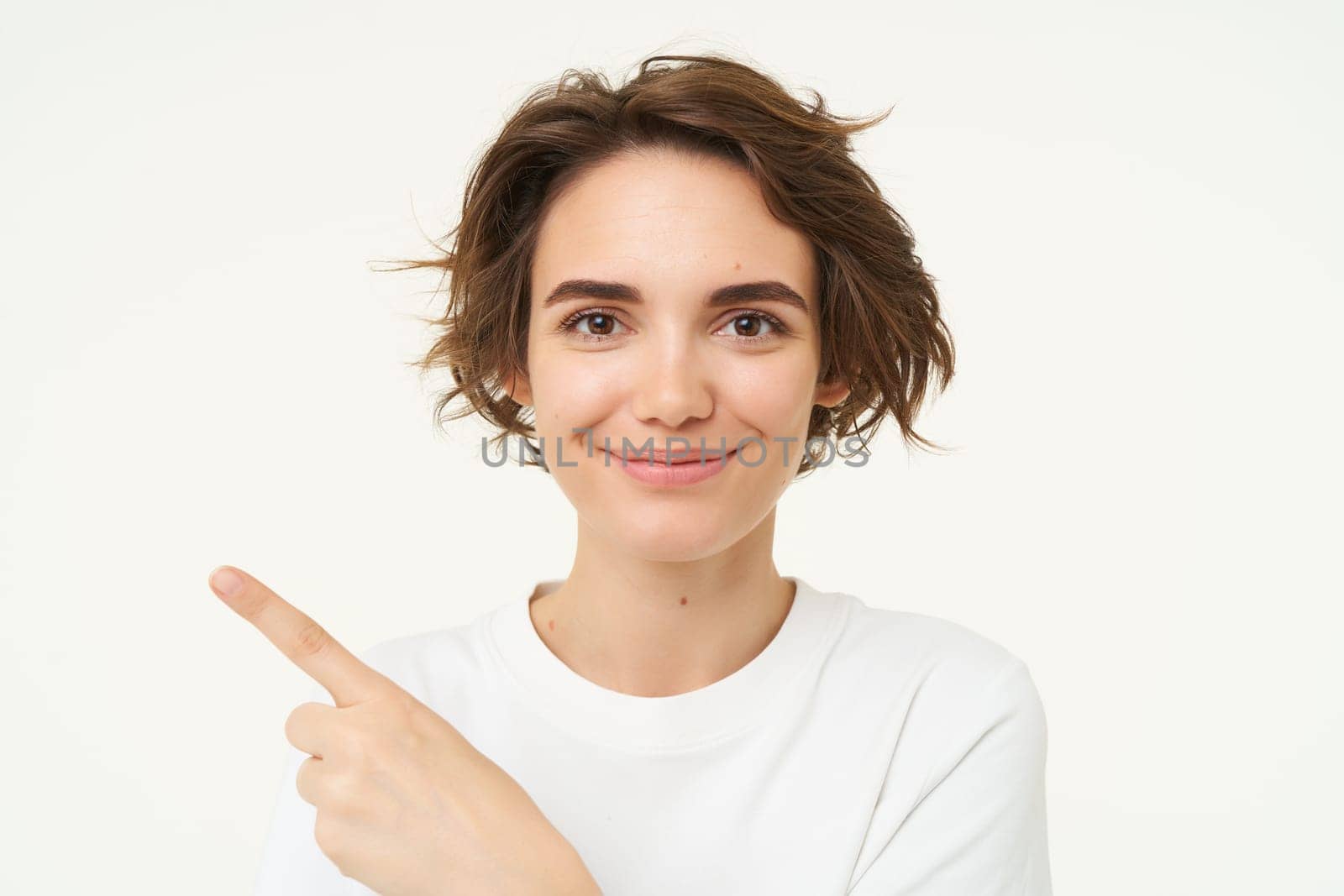 Close up shot of happy, candid woman, laughing and smiling, pointing finger left, showing advertisement, standing over white background by Benzoix